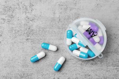 Pills spilling with open daily pill organizer on a grey concrete background, top view, copy space