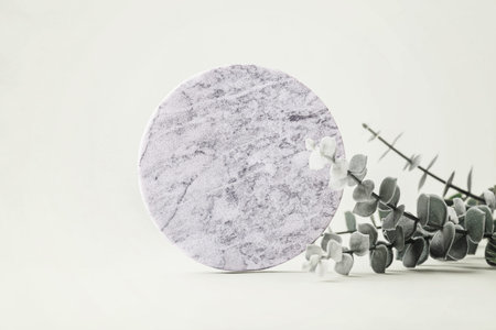 Empty round marble podium with green leaves on light green background for product display, cosmetic, perfume, jewelry, or skincare product mockups and presentations