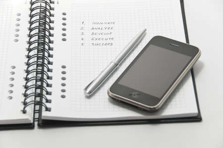 Iphone 3G and elegant silver pen on white spiral notebook (important business steps written on page)のeditorial素材