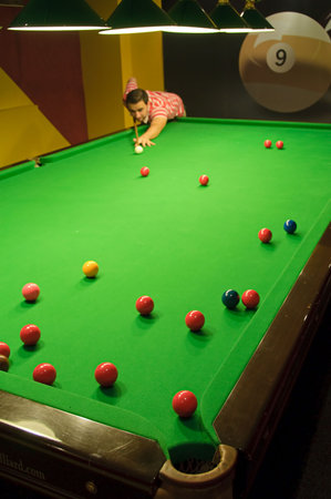 Young man playing snooker in a pub (balls scattered on the table) (view from a pocket)