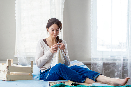 young beautiful woman knits a sweater sitting on the bedの写真素材