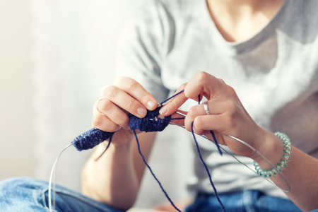 A young woman knits with a knitting sweater of natural wool. Smiling, close-up