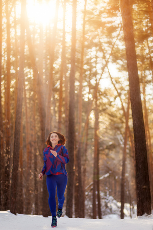 A woman running in the winter forest sunsetの写真素材