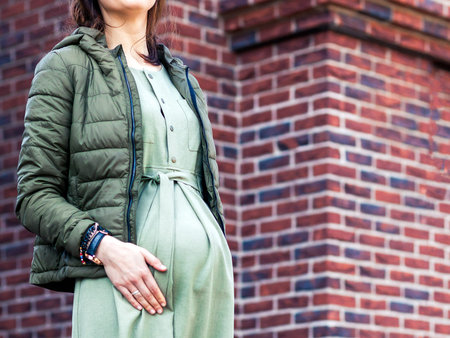 Close-up of a pregnant belly. A pregnant summer day in a green jacket and summer dress