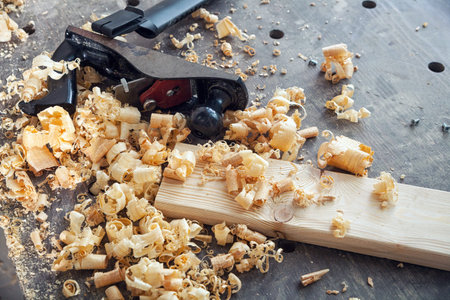 A black jack plane for a tree lies on a wooden table around a lot of wooden sawdust