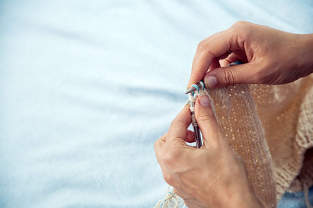 Close-up Young woman knits with knitting needles from pink woolen thread warm winter scarf on blue...