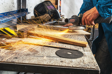 An adult male in a blue uniform   grinder metal an angle grinder  on a wooden table in the workshop,...