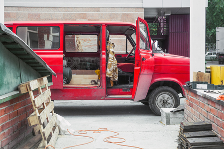 A red old van with open doors for travel and work is parked on a construction site on a summer day, against a background of wooden structures and building materialsの写真素材