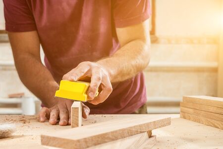 Close up  A man carpenter  is sanding a wooden on the wooden table in the workshop, on the table there are many wooden barsの写真素材