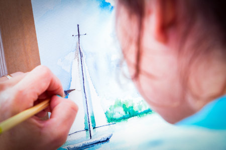 Close-up woman artist paints a thin wooden brush and watercolor drawing a yacht in the sea in an album for drawingの写真素材