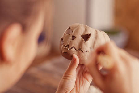 Close-up Beautiful Woman Artist doing on a clay pumpkin face jack for Halloween on a wooden table in the workshop, preparing for Halloweenの写真素材