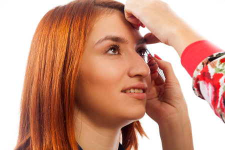 The master on the eyebrows corrects the shape of the roach with tweezers  red-haired beautiful woman...