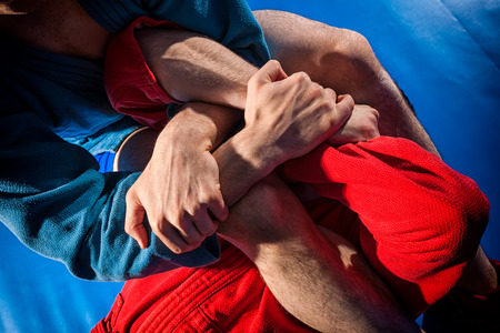 Man wrestlers of grappling and jiu jitsu in a blue and red kimono makes submission wrestling.Fighting techniques:   armbar, armlockの写真素材