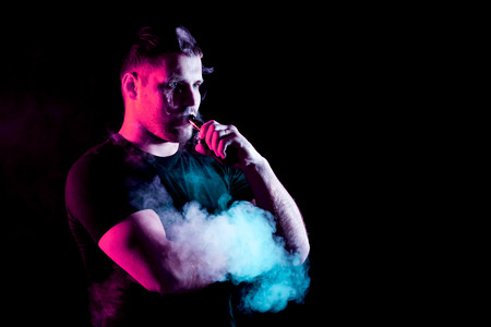 vaping man holding a mod. A cloud of vapor. Black background.の写真素材
