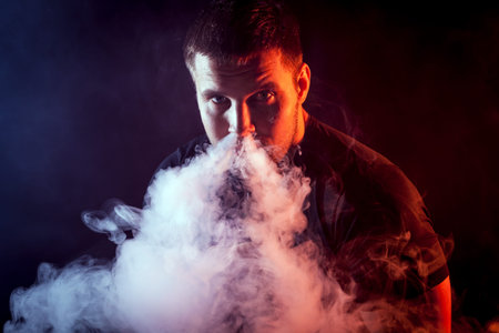 The man smoke an electronic cigarette on the dark backgroundの写真素材