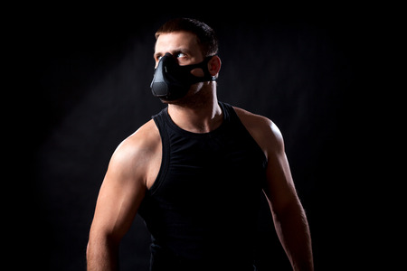 A dark-haired man athlete in a black training mask, a sports shirt pensively looking at a black isolated backgroundの写真素材