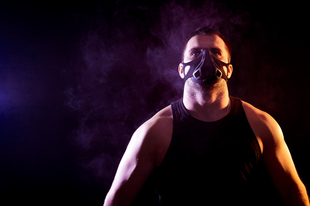 Portrait of young athletic man wearing  sport shirt and training mask  on black isolated background, around blue smoke from a vapeの写真素材