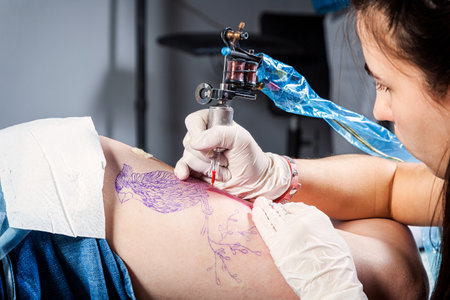 Close up of the tattooist making by professional artist is tattooing body woman using machine in a creative design work studioのeditorial素材