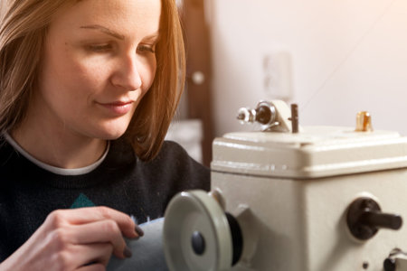 Sewing process of the female fur coat. Close up of a young cheerful woman furrier smiles and sews a...