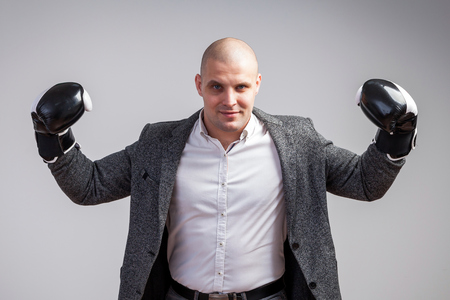Young bald man in white shirt, gray suit and boxing gloves smiling, showing biceps on white isolated backgroundの写真素材
