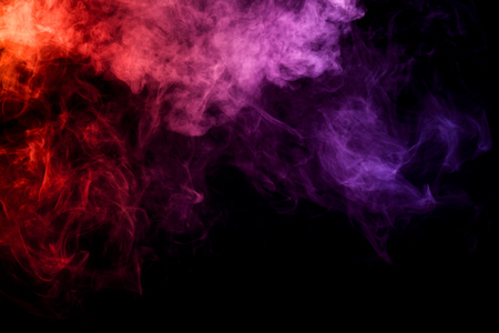 Thick colorful smoke of  orange and pink on a black isolated background. Background from the smoke of vapeの写真素材