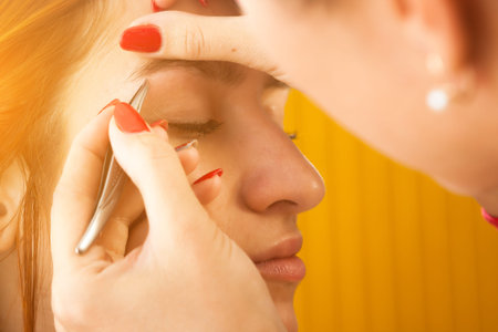 Close up of the master on the eyebrows corrects the shape of the roach with tweezers  red-haired...