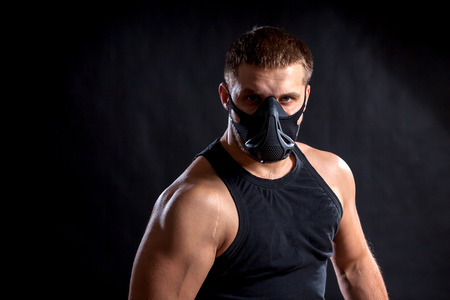 Portrait of a  dark-haired man athlete in a black training mask, a sports shirt on a black isolated backgroundの写真素材