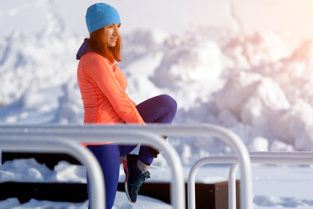 Young woman in bright sports clothes doing stretching before running on a sports field on a bright winter dayの写真素材