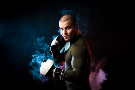 A strong dark-haired sportman  in a green sports shirt and black and white boxing gloves  posing ...