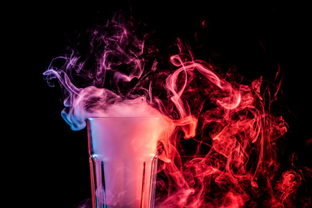 Close up of a  transparent  glass filled with a cloud from a  red vape smokes and stands on a black isolated backgroundの写真素材
