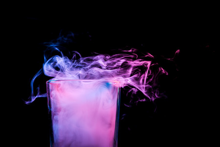 A close-up glass transparent glass filled with a wig from a pink vape smokes and stands on a black isolated background. Glass bongs for smoking soft focus.の写真素材