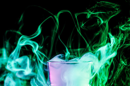 A close-up glass transparent glass filled with a wig from a  green vape smokes and stands on a black isolated background. Glass bongs for smoking soft focus.の写真素材