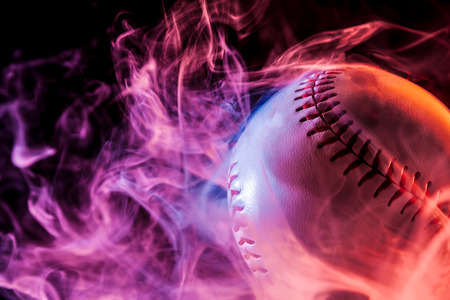 Close up of a white baseball ball in multi-colored red smoke from a vape on a black isolated backgroundの写真素材