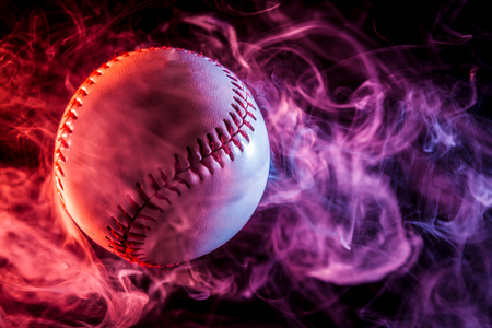 Colorful baseball ball in multi-colored red smoke from a vape on a black isolated backgroundの写真素材