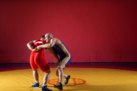 Two greco-roman  wrestlers in red and blue uniform making a suplex wrestling  on a yellow wrestling carpet in the gymの写真素材
