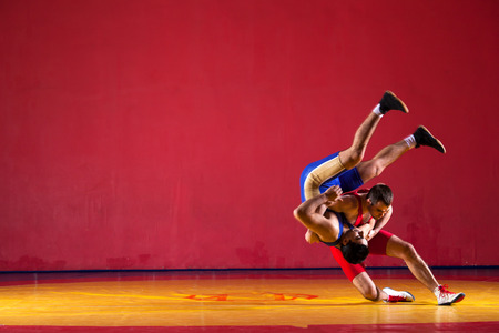 Two greco-roman  wrestlers in blue uniform wrestling   on a yellow wrestling carpet in the gymの写真素材