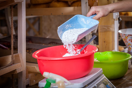 Close-up of a woman baker pouring a large spoon of white flour into a basin