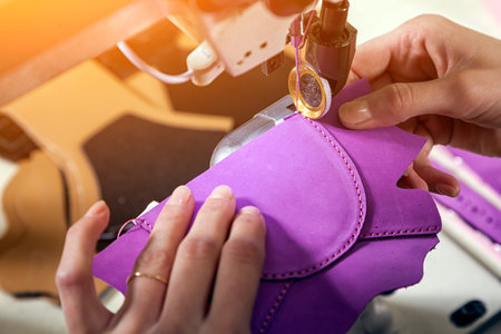 Close-up of a young woman working as a seamstress in a purple unifrome sews genuine leather...