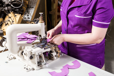 Close-up of a young woman working as a seamstress in a purple unifrome sews genuine leather...