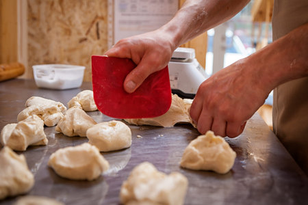 A close-up of a male baker  pulls out the dough for cooking buns wiith cheese on a knotted table...