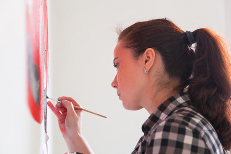 Young woman painter and mother boy draws for a child on a white wall a beautiful red car in a light children's roomの写真素材
