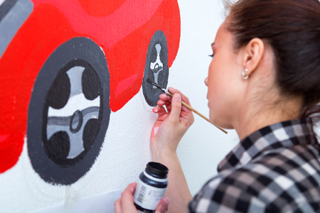 Young woman painter and mother boy draws for a child on a white wall a beautiful red car in a light children's roomの写真素材