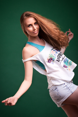 Beautiful young blonde woman in white top in denim shorts smiling and posing on a black isolated backgroundの写真素材