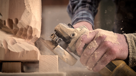 Experienced carpenter in work clothes    saws a man's head with a tree , using an angle grinder  in the workshop, carpenter's hands in sawdustの写真素材