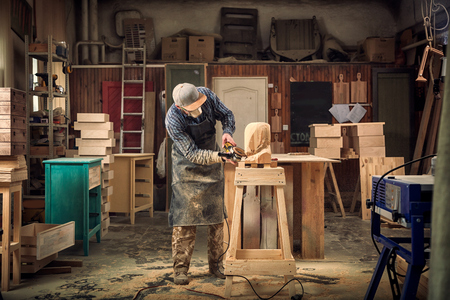 Ð¡arpenter,small buiness owner in work clothes saws a man's head with a tree , using an angle grinder  in the workshop, around a lot of tools,wooden,furniture for workの写真素材