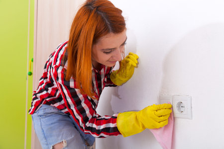  Ð¡lose up of young woman  in jeans, yellow gloves and plaid shirt  is wiping the switches and the...