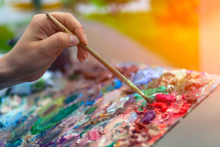 A close-up artist paints on a canvas an urban landscape of a summer embankment with atractions of oil paintsの写真素材