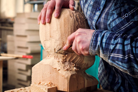 Close up young man carpenter in a work clothes  saws a man's head with a tree , using a chisel  in the workshop, around a lot of tools for workの写真素材