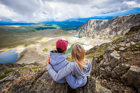 Atmospheric moment for lovers in the mountains. Hiking woman and man with backpack is sitting on the...