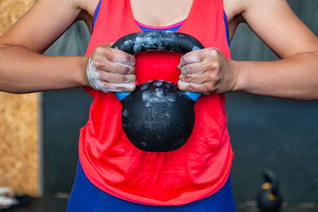 Close-up A young woman in a pink top holds the weights at the chest level, hands in magnesia.の写真素材